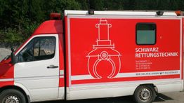 Rotes Fahrzeug mit Logo und Schriftzug "Schwarz Rettungstechnik" an der Seite, Wald im Hintergrund.