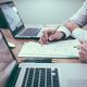 Due persone lavorano al computer con documenti e appunti su una scrivania.