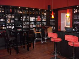 Moderne Bar mit roten Hockern, dunklen Regalen voller Flaschen und warmem Licht.