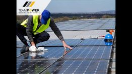 Operaio installa pannelli solari su un tetto. Cielo limpido e paesaggio in lontananza.