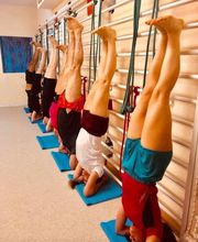 Personas practicando yoga en inversión con cuerdas, alineadas junto a una pared en un estudio.
