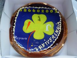 Tarta de aniversario con diseño de trébol verde y texto, en una caja blanca.