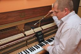 Mann stimmt ein Klavier mit Werkzeug; auf den Tasten liegt ein Stimmgerät.