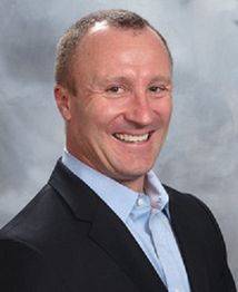 Smiling man in a suit against a gray background.