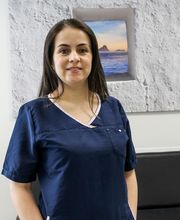 Mujer con uniforme médico azul, parada en una sala con un cuadro de paisaje en la pared.