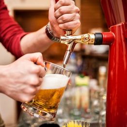 Pouring beer from a tap into a glass with a frothy head in a bar setting.
