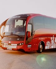 Autobús rojo en carretera rural al atardecer.