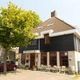 Een hoekgebouw met zwart-witte gevel en een terras onder een boom.