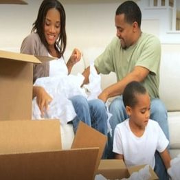 Family unpacking boxes, sitting on a sofa, surrounded by cardboard and packing material.