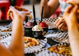 People enjoying pizza and ice cream at a table with black and white checkered paper.