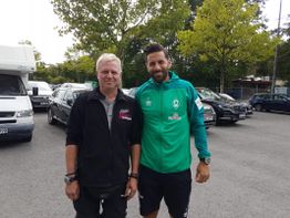 Zwei Männer stehen auf einem Parkplatz, einer trägt eine grüne Werder Bremen Jacke.