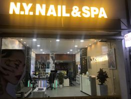 Außenansicht eines hell erleuchteten N.Y. Nail & Spa Salons bei Nacht mit moderner Einrichtung.