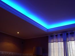 Teto iluminado em azul, lâmpada acesa e cortina clara em um canto da sala.