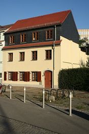 Gelbes, dreistöckiges Haus mit rotem Dach und Holzfensterläden, bei sonnigem Wetter fotografiert.