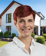 Eine lächelnde Frau mit kurzen roten Haaren steht vor einem modernen weißen Haus mit Garten.