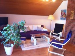 Wohnzimmer mit lila Sofa, Pflanzen, Tisch und zwei Sesseln unter Dachschräge.