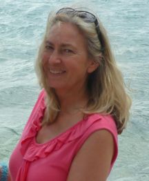 Frau mit blonden Haaren und Sonnenbrille lächelt am Strand, trägt ein pinkes Oberteil.