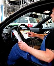 Mechaniker im Auto bedient Laptop zur Fahrzeugdiagnose in einer Werkstatt.