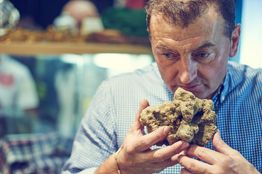 Uomo annusa un tartufo marrone, tenendolo vicino al viso, con espressione concentrata.