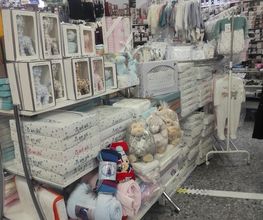 Estantería con ropa y accesorios de bebé en una tienda iluminada.