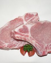 Zwei rohe Koteletts auf weißem Hintergrund, dekoriert mit Tomatenstücken und Petersilie.