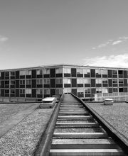 Schwarz-weiß Foto eines modernen Gebäudes mit quadratischen Fenstern und einem Steg im Vordergrund.