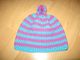 Bunte gestrickte Mütze mit Streifen in Blau und Pink auf einem Holzboden.
