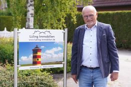 Eine Person steht lächelnd neben einem Schild mit der Aufschrift "Lüling Immobilien".