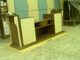 Holzschrank in Werkstatt mit offenen Regalen und zwei weißen Türen auf einer Holzplatte.