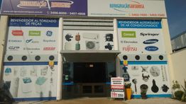 Fachada de loja de refrigeração com cartazes de marcas de peças e ar-condicionados na entrada.