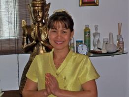 Frau in gelber Kleidung lächelt, steht vor einer Buddha-Statue und hält die Hände gefaltet.