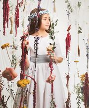 Niña con corona de flores, rodeada de flores suspendidas, mira hacia la derecha.