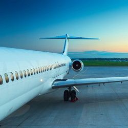 Airplane on tarmac at sunset with blue sky and distant horizon.