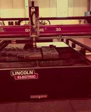 Máquina de corte industrial Lincoln Electric en un taller, con herramientas sobre la mesa.