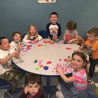 Children sitting around a table, playing with colorful toys and shapes, smiling and having fun.