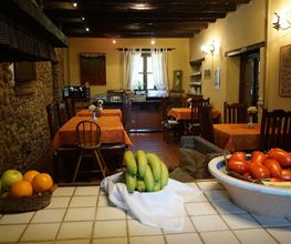Comedor rústico con mesas naranjas, frutas en la barra y ambiente cálido.