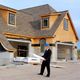 Man in suit and blue helmet examining house construction plans outside a new build site.