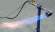 Bruciatore a gas acceso su un supporto blu con fiamma blu e arancione su sfondo grigio.