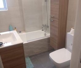 Baño moderno con lavabo, inodoro, bañera y mueble de madera. Luz natural por una ventana.