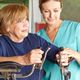 Elderly woman in rehab with a caregiver, using exercise equipment indoors.