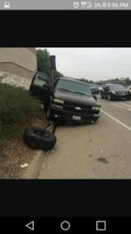 SUV with front tire off, parked on road shoulder beside greenery and open driver-side door.
