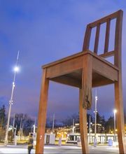 Großer Holzstuhl mit einem gebrochenen Bein auf einem Platz bei Abenddämmerung.