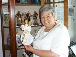 Eine Frau hält eine Engelsfigur vor einer Vitrine mit weiteren Figuren.