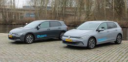 Twee grijze auto's geparkeerd bij een waterkant, met "Lesauto" op de zijkanten.