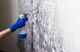 Gloved hand spraying cleaning solution on a moldy wall.