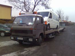Ein Abschleppwagen transportiert einen weißen Van auf einem grauen Industriegelände.