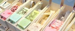 Handgemachte Seifen in Holzkisten, farbenfroh in Rosa, Grün und Beige sortiert.