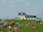 Menschen entspannen auf einer grünen Wiese vor einem großen, weißen Gebäude an einem sonnigen Tag.