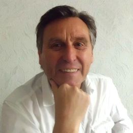 Ein lächelnder Mann in weißem Hemd stützt sein Kinn auf seine Hand.