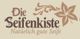 Logo mit Schriftzug: "Die Seifenkiste - Natürlich gute Seife" und floralen Verzierungen.
